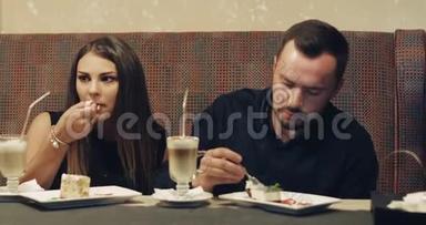 一对年轻夫妇坐在咖啡馆里，用勺子互相喂一个美味的蛋糕A。